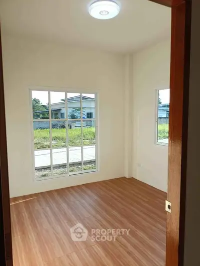Bright room with wooden flooring and large windows offering natural light and garden view.
