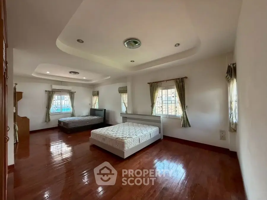 Spacious bedroom with wooden floors and two beds in a well-lit room.
