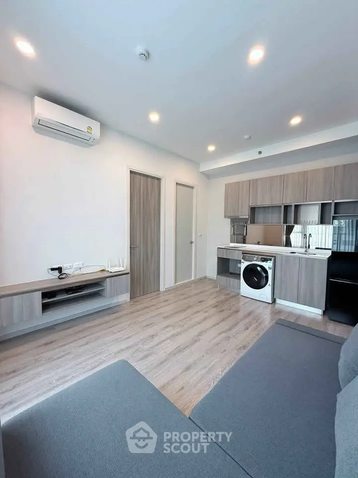 Modern living room with open kitchen, featuring sleek appliances and stylish wood flooring.