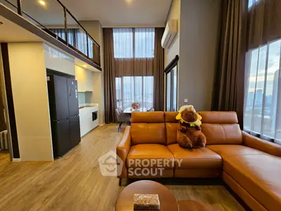 Spacious modern living room with high ceilings and large windows offering city views, featuring a leather sofa and open kitchen.