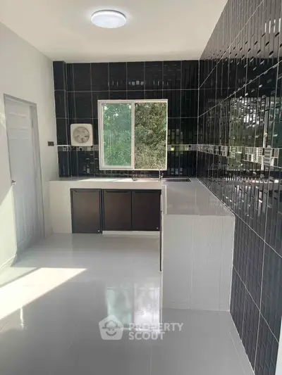 Modern kitchen with sleek black tiles and large window offering natural light.