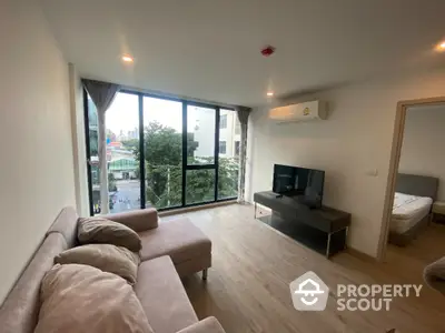 Modern living room with large windows and city view, featuring cozy seating and sleek TV setup.