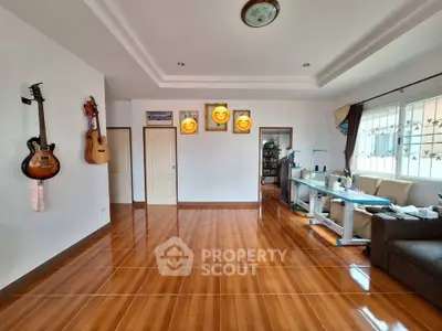 Spacious living room with wooden flooring and natural light, featuring guitars and modern decor.