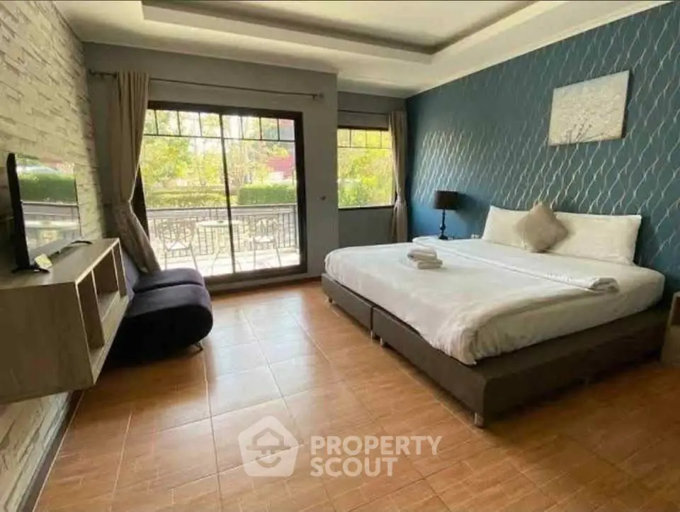 Spacious bedroom with modern decor and large window overlooking balcony.