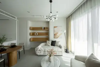 Modern living room with elegant decor and natural light, featuring a stylish chandelier and cozy seating area.