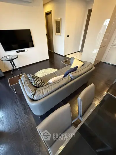 Modern living room with sleek furniture and dark wood flooring, featuring a stylish sofa and wall-mounted TV.