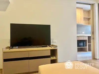 Modern living room with sleek TV setup and view into stylish kitchen area.