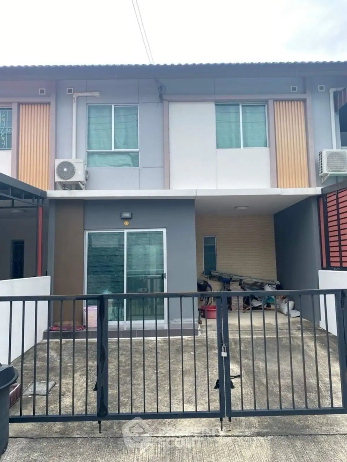 Modern townhouse exterior with gated entrance and air conditioning units.