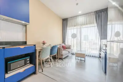 Modern living room with blue kitchen cabinets and cozy seating area, featuring large windows with city view.