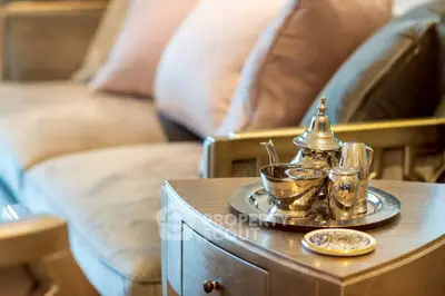 Elegant living room with luxurious silver tea set on wooden table, plush cushions in background.