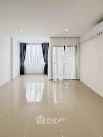 Spacious empty living room with large windows and elegant curtains.