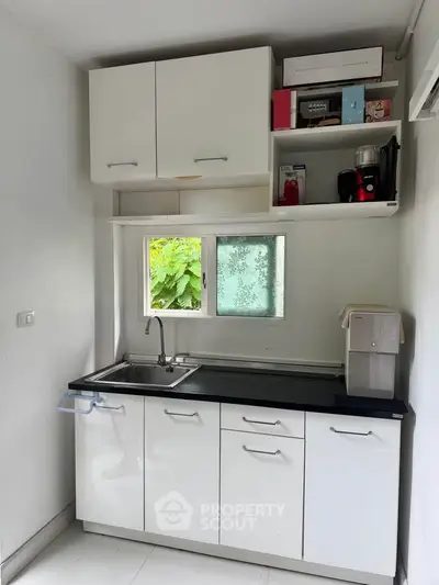 Compact kitchen with white cabinets and countertop, featuring a sink and small appliances, ideal for efficient cooking.