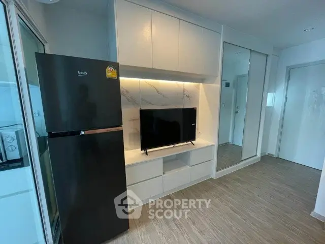 Modern living room with sleek TV unit and refrigerator, featuring stylish wood flooring and ample storage.