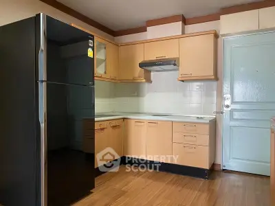 Modern kitchen with sleek black fridge and wooden cabinets in cozy apartment