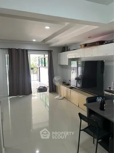 Spacious living room with modern decor and large TV, leading to a balcony with natural light.