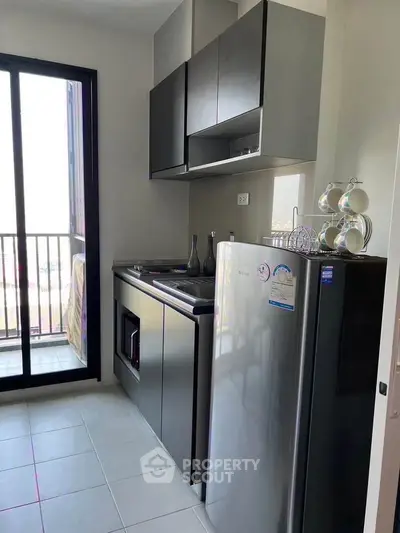 Modern kitchen with sleek cabinets and stainless steel fridge near balcony.