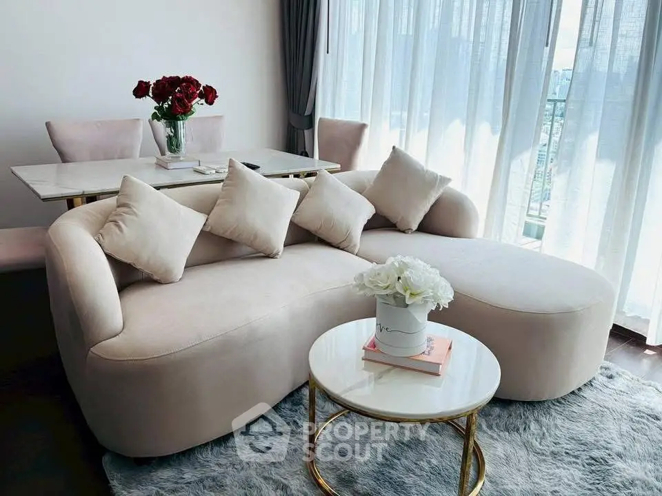 Elegant living room with plush sofa, chic decor, and natural light through sheer curtains.