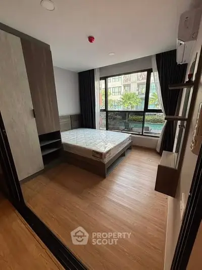 Modern bedroom with large window and wooden flooring in urban apartment