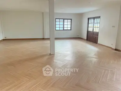 Spacious open-plan living area with wooden flooring and large windows.