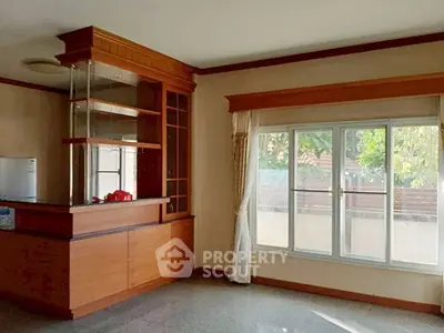 Spacious living room with large window and wooden cabinetry, perfect for natural light lovers.