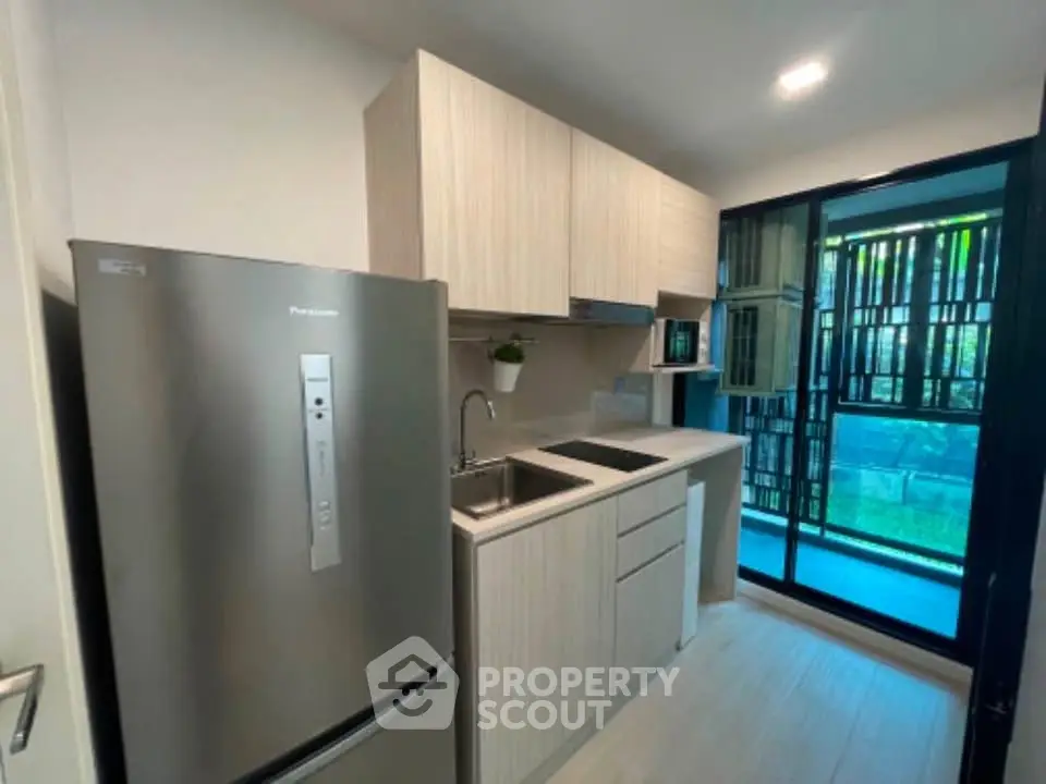 Modern kitchen with sleek cabinetry and stainless steel fridge, featuring a large window for natural light.