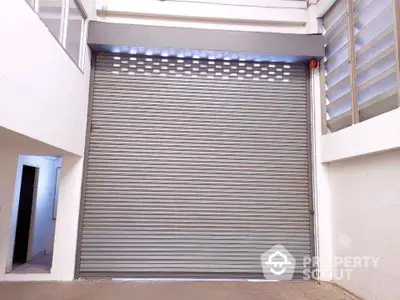 Spacious industrial warehouse with large roller shutter door and ample natural light.