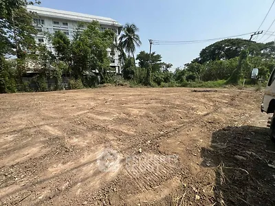Vacant land plot with potential for development, surrounded by lush greenery and nearby buildings.
