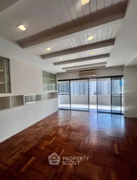 Spacious living room with parquet flooring and large windows offering city views.