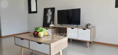 Modern living room with stylish TV stand and fruit centerpiece on coffee table.