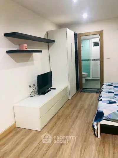 Modern studio apartment with wooden flooring and sleek furniture, featuring a cozy bed and compact TV setup.