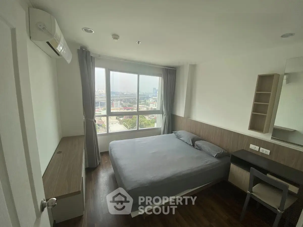 Modern bedroom with large window offering city view, featuring sleek furniture and minimalist design.