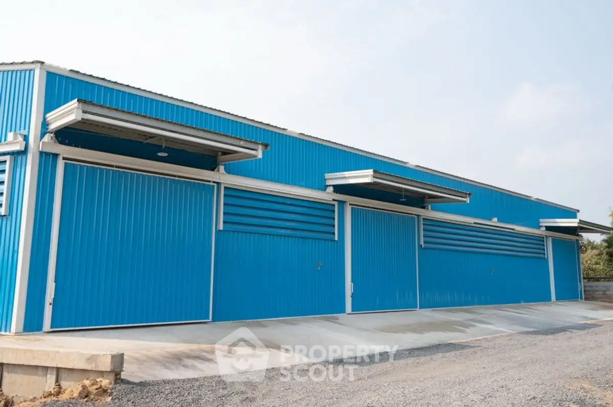 Modern blue industrial warehouse with large sliding doors and spacious driveway.