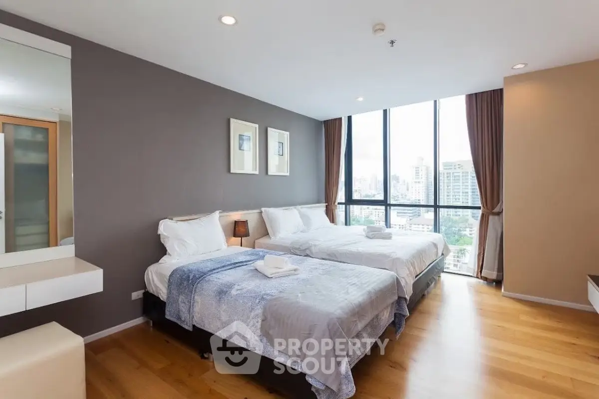 Spacious bedroom with two beds and city view, featuring modern decor and large windows.