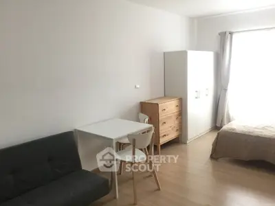 Minimalist bedroom with natural light, featuring a bed, wardrobe, and small dining area.