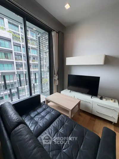 Modern living room with sleek black leather sofa and large TV, featuring a view of urban architecture through glass doors.