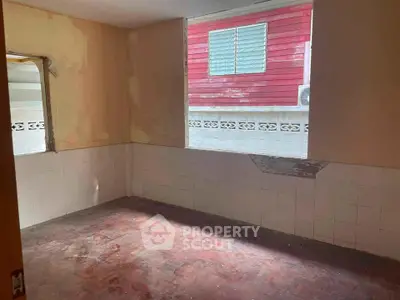 Spacious room with large window and tiled walls, ideal for renovation.