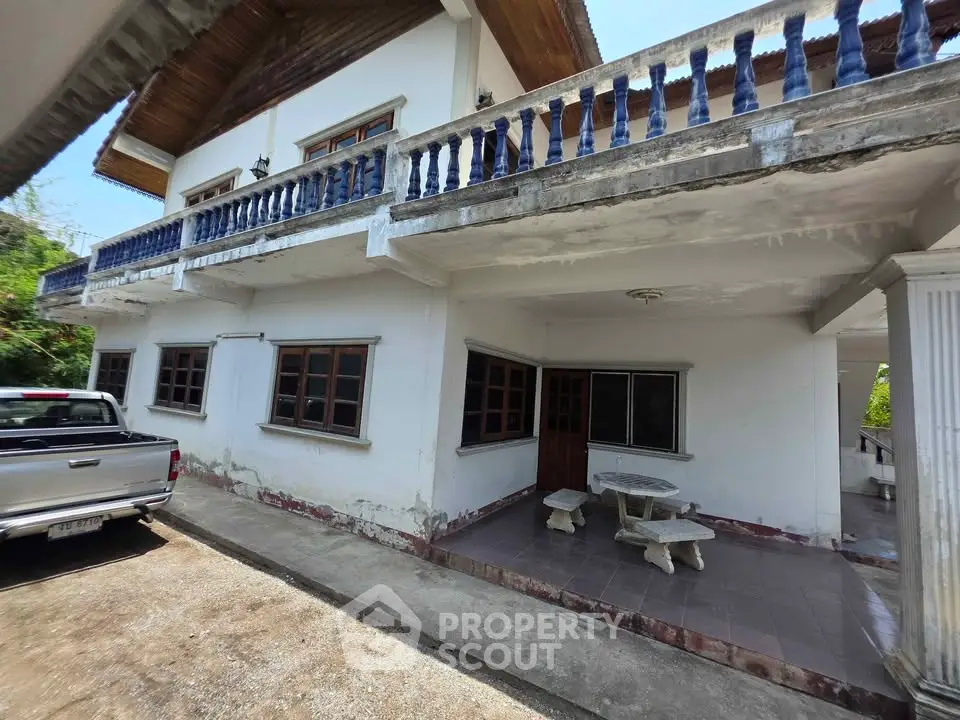 Charming two-story house with spacious balcony and outdoor seating area, perfect for family living.