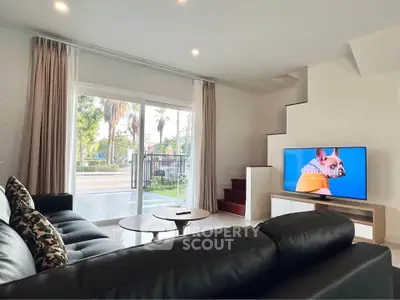 Modern living room with sleek black sofa and large sliding glass doors opening to garden view.