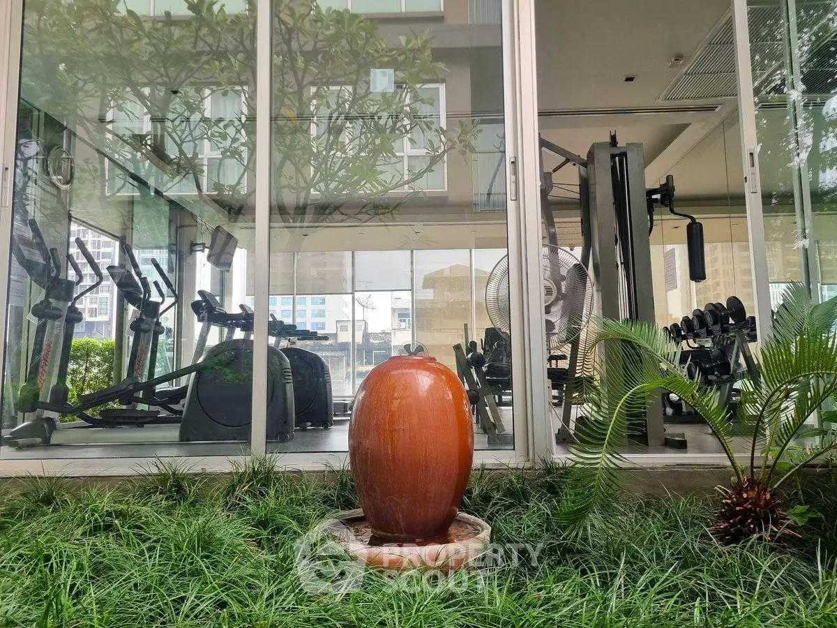 Modern gym with exercise equipment and large windows overlooking greenery.