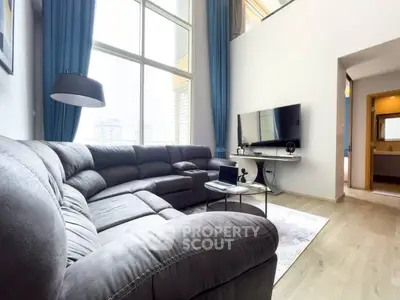 Spacious modern living room with high ceilings and large windows, featuring a cozy sectional sofa and sleek entertainment setup.