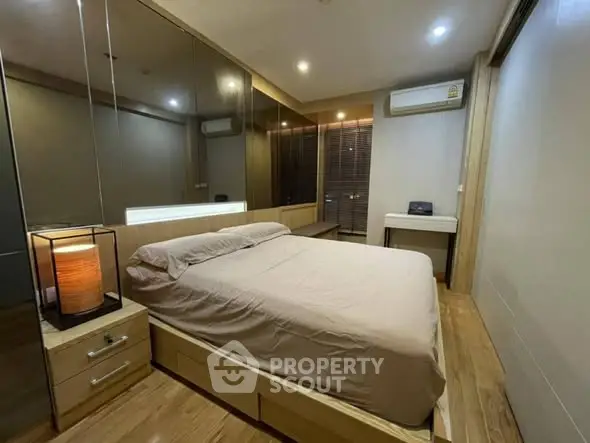 Modern bedroom with mirrored wall and wooden flooring, featuring a cozy bed and ambient lighting.