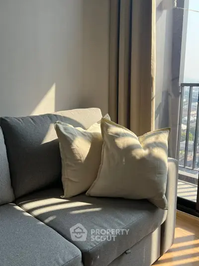 Cozy living room with sunlight streaming on a modern gray sofa and balcony view.