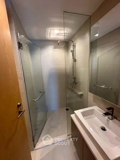 Modern bathroom with glass shower enclosure and sleek vanity in contemporary apartment.
