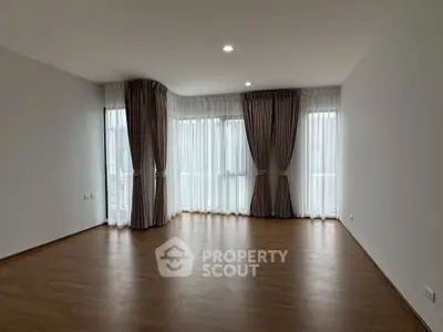 Spacious empty living room with large windows and elegant curtains, perfect for natural light.