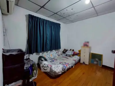 Cozy bedroom with wooden flooring and a single bed, featuring dark curtains and a simple dresser.