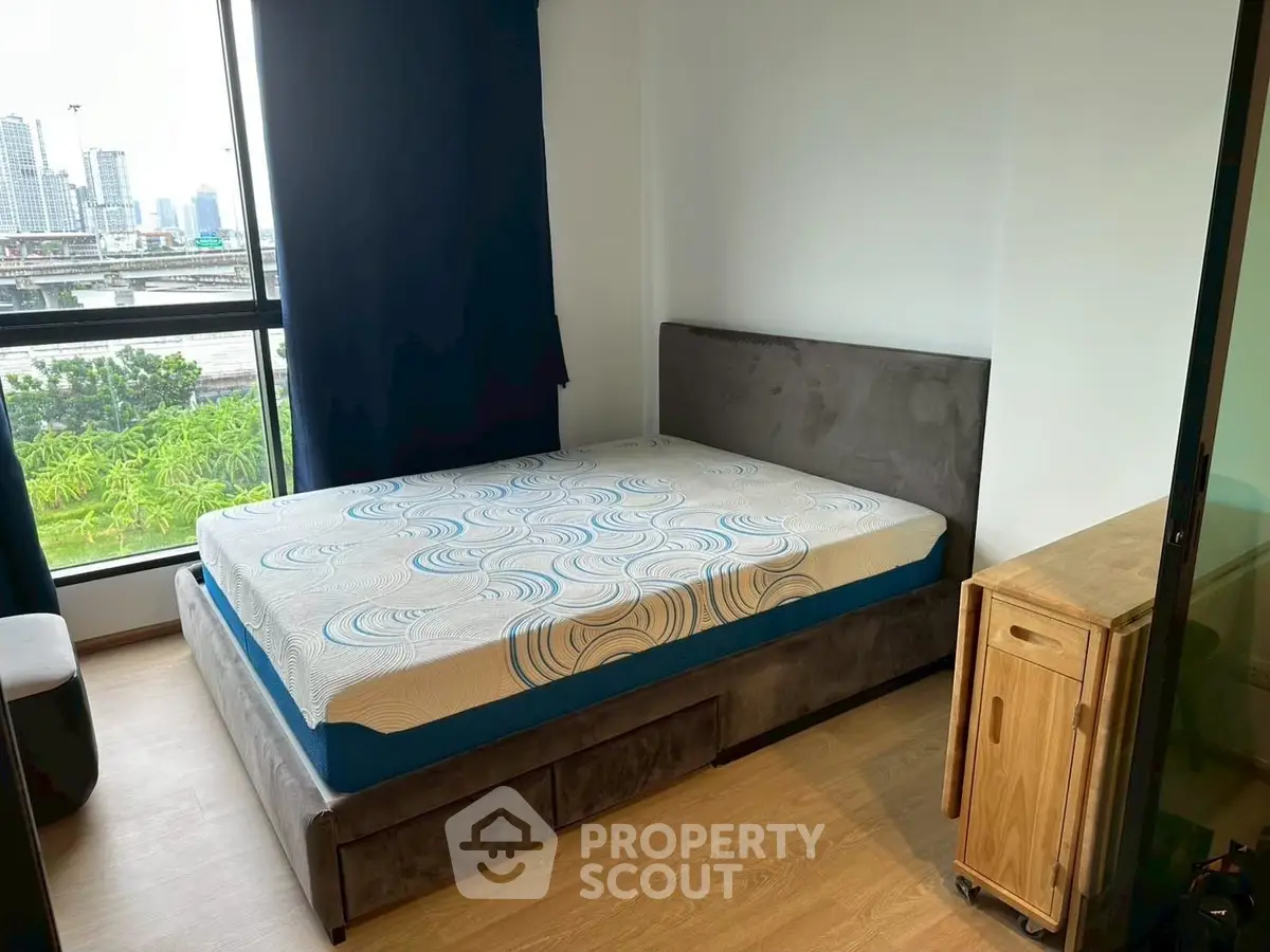 Modern bedroom with large window and city view, featuring a stylish bed and wooden side table.
