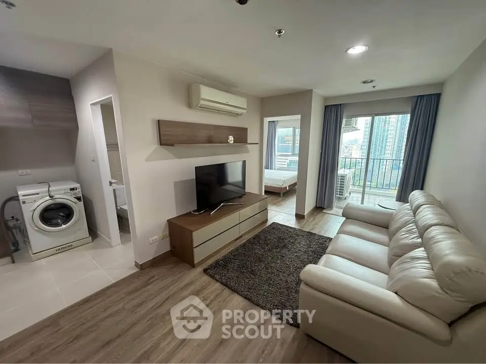 Modern living room with open layout, featuring a cozy sofa, TV, and washing machine, overlooking city views.