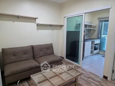 Cozy living room with brown sofa and glass coffee table, adjacent to compact kitchen.