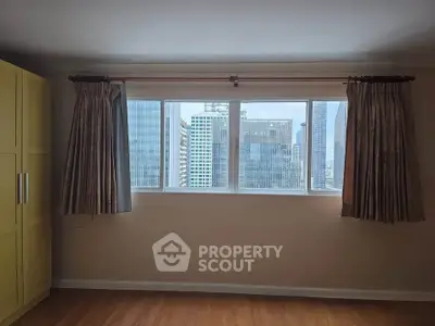 Spacious room with large window offering stunning city skyline view, perfect for urban living.