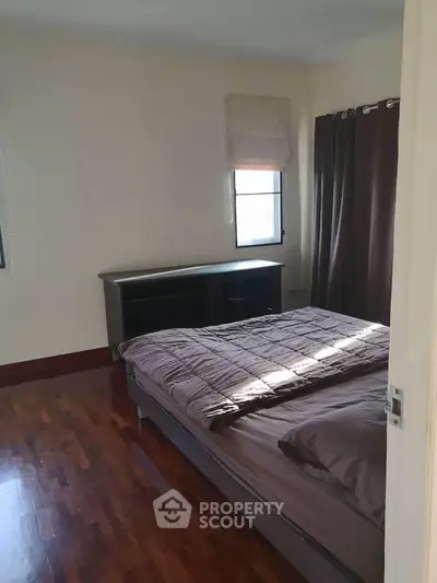 Cozy bedroom with wooden flooring and natural light, featuring a comfortable bed and elegant curtains.